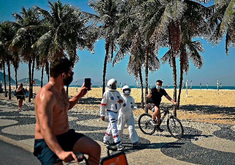 Men riding bikes take pictures of Brazilian accountant Tercio Galdino, 66, and his wife Ailicea who walk along Copacabana beach wearing protective suits, in Rio de Janeiro, Brazil.(Photo by Carl de Souza/AFP Photo)